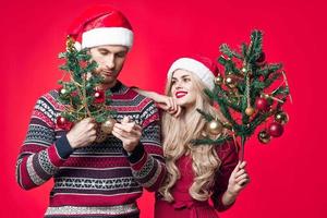 alegre jovem casal dentro Novo ano roupas decoração brinquedos vermelho fundo foto