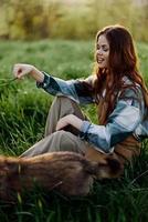 feliz mulher sentado dentro natureza e jogando com dela animal dentro a parque sentado em a verde Relva foto