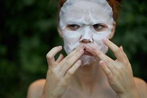agradável mulher anti-rugas mascarar pressione seu dedos perto a lábios dermatologia verde arbustos fundo foto