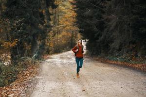 enérgico mulher corrida ao longo a estrada com mochila dentro outono floresta foto