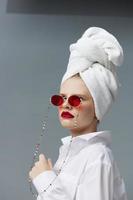 bonita mulher vermelho oculos de sol cosméticos com toalha em cabeça cinzento fundo foto