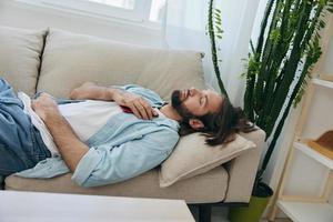 uma homem dormindo em a sofá durante a dia é cansado e relaxado depois de estresse e sentindo-me ruim. estresse às trabalhar, pobre dormir e saúde problemas foto