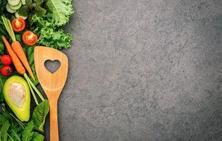 alimentos saudáveis e conceito de cozinha com uma espátula de madeira e vegetais no fundo de pedra escura. foto