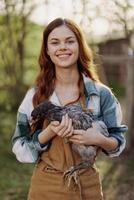 uma feliz jovem mulher sorridente e segurando uma jovem frango este lays ovos para dela Fazenda foto