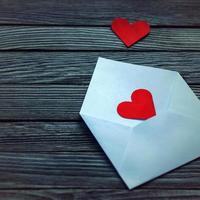 branco enviar envelope e dois vermelho papel corações em uma cinzento de madeira BA foto