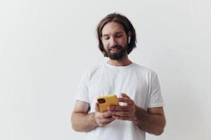 homem blogueiro detém uma telefone dentro dele mãos e comunica com pessoas conectados dentro social redes com uma sorrir e uma branco camiseta em uma branco fundo foto