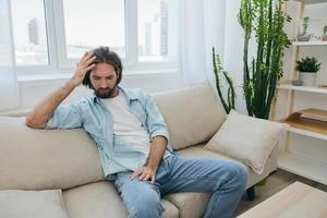 uma jovem masculino trabalhador autonomo senta em a sofá depois de uma exigente trabalho e descansos Infelizmente inclinado em a sofá. foto