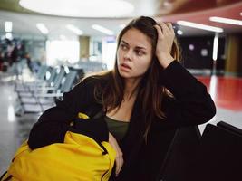 cansado mulher atrás uma ouro mochila aeroporto esperando para uma voar foto