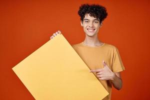 alegre cara com encaracolado cabelo amarelo poster dentro mãos estúdio publicidade foto