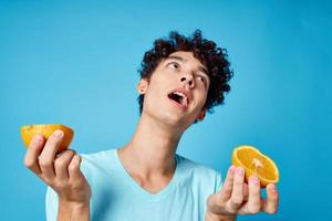 alegre homem com encaracolado cabelo segurando laranjas fruta azul fundo foto