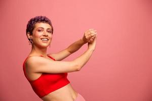 moda retrato do uma mulher com uma curto corte de cabelo do roxa cor e uma sorrir com dentes dentro uma vermelho topo em uma Rosa fundo felicidade foto