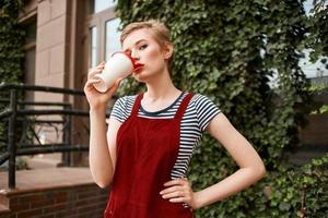 bonita mulher com uma copo do beber em a rua perto a arbustos foto