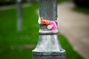 perdido Rosa ortodôntico chupeta suspensão amarrado para uma rua luz pólo dentro uma parque perto areia caminho e gramado foto