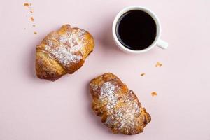 branco copo do café e dois croissants em a Rosa pastel cor fundo. plano deitar, topo Visão foto