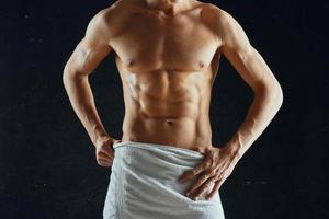 desportivo homem com uma bombeado muscular corpo dentro uma toalha Sombrio fundo foto