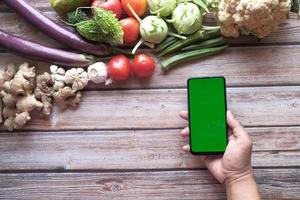 Smartphone com tela verde em fundo de madeira com muitos vegetais frescos foto