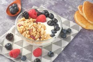 granola com iogurte e frutas vermelhas em uma tigela em fundo neutro