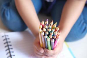 close-up da mão de uma criança segurando muitos lápis coloridos