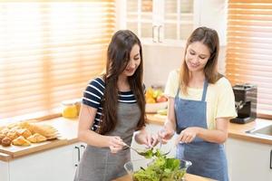 feliz e sorrir lésbica casal cozinhando salada dentro a cozinha. salada dentro vidro tigela com doce sorrir enquanto cozinhando junto. orgulho mês para promover igualdade e diferenças do homossexual. foto