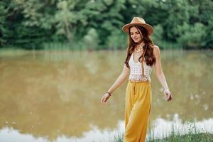 lindo mulher dentro uma chapéu e vestido ecológico hippie Veja ao ar livre de a lago caminhando foto