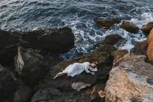 sensual mulher dentro grandes branco vestir molhado cabelo deitado em uma rochoso penhasco panorama foto