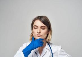 emocional mulher dentro azul médico luvas toques dela cabeça com dela mãos em uma luz fundo foto