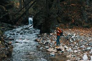 mulher viaja de a rio dentro a montanhas e uma mochila em dela costas transparente água floresta foto