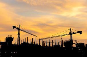 silhuetas do construção construção local e construção guindastes com pôr do sol fundo foto