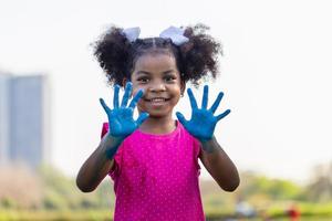 alegre pequeno criança menina mostrando pintado mão, fofa pequeno criança menina jogando ao ar livre dentro a jardim foto
