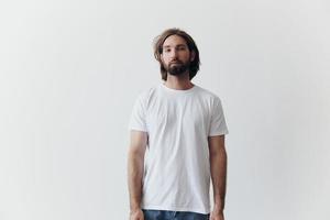 retrato do uma homem com uma Preto Grosso barba e grandes cabelo dentro uma branco camiseta em uma branco isolado fundo emoção do tristeza e anseio foto