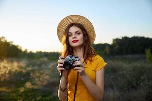 mulher dentro uma chapéu com uma Câmera dentro dela mãos vermelho lábios atraente Veja natureza foto