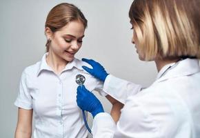 médico mulher com uma estetoscópio detém uma paciente de a ombro em uma luz fundo foto