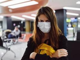 mulher com desapontado facial expressão vestindo médico mascarar senta às a aeroporto foto