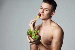 alegre homem com muscular tronco vegetal salada comendo saúde Comida cortada Visão foto