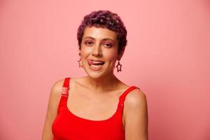 moda retrato do uma mulher com uma curto corte de cabelo do roxa cor e uma sorrir com dentes dentro uma vermelho topo em uma Rosa fundo felicidade foto