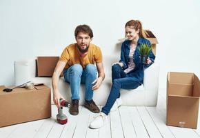 jovem casado casal dentro uma Novo apartamento em uma branco sofá caixas com coisas comovente foto