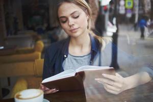 mulher lendo livro cafeteria período de férias estilo de vida copo do café dentro a manhã foto