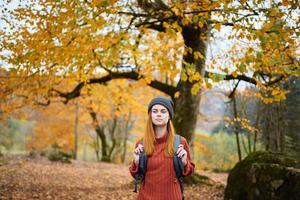 mulher com uma mochila anda em dentro a outono floresta amarelo folhas natureza foto