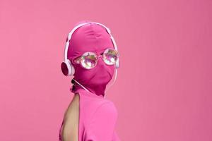 criativo ventilador arte foto do uma jovem fêmea cyberpunk blogueiro em uma Rosa fundo vestindo uma Rosa rosto inteiro mascarar com brilhando volta óculos e fones de ouvido