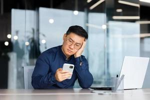 retrato do uma preocupado jovem ásia homem olhando Infelizmente às a telefone. entediado, recebido mau notícia foto