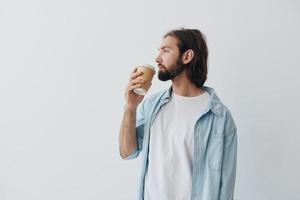 freelance milenar homem com barba bebendo café a partir de uma caranguejo copo dentro à moda hipster roupas em uma branco fundo foto