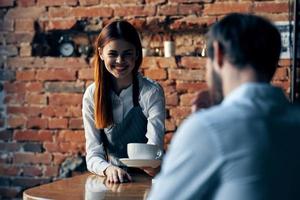 bonita mulher garçom traz café serviço tijolo parede foto