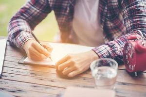 mão escrevendo dentro caderno moedas e alarme relógio para fundo foto