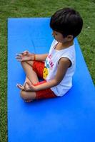ásia inteligente criança fazendo ioga pose dentro a sociedade parque ar livre, crianças ioga pose. a pequeno Garoto fazendo ioga exercício. foto