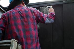 foco na mão do trabalhador pintando a cor preta na cerca de aço foto