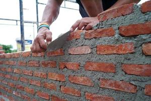 closeup mãos de trabalhador instalando os pedreiros para construir a parede no canteiro de obras. foto