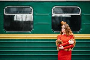 jovem com cabelo ruivo em um vestido vermelho brilhante perto de um velho carro de passageiros foto