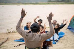 costas Visão às africano homem ter Diversão jogando guitarra com amigo acampamento às a de praia. cantando , rindo, jogando guitarra foto