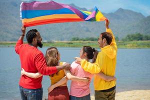 costas visualizar. jovem diversidade pessoas tendo Diversão segurando lgbt arco Iris bandeira em a de praia. apoiantes do a lgbt comunidade foto