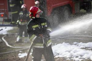 bombeiros extinguir uma fogo. uma equipe do bombeiros em uma fundo do fumaça e uma fogo motor foto